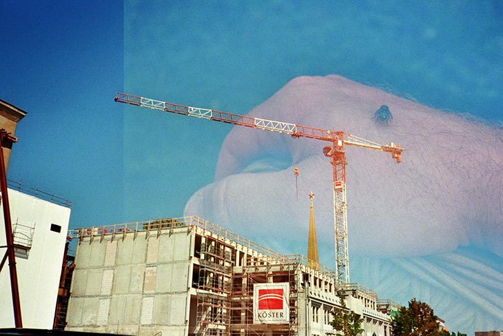 eine Doppelbelichtung: Fliege auf einer Hand, dazu eine Baustelle mit Kran