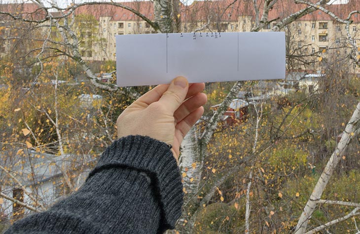 Hand hält ein Stück Papier als Entfernungsmesser