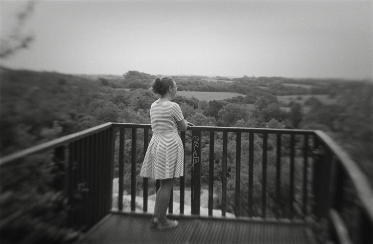 Eine Frau steht auf einer Ausblicksplattform und schaut in die Landschaft.