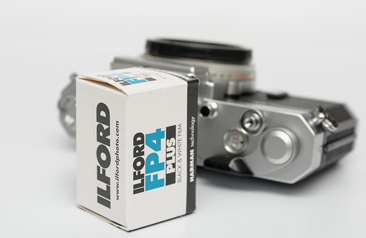 Filmschachtel vom Ilford FP4 Plus und analoge Kamera im Hintergrund