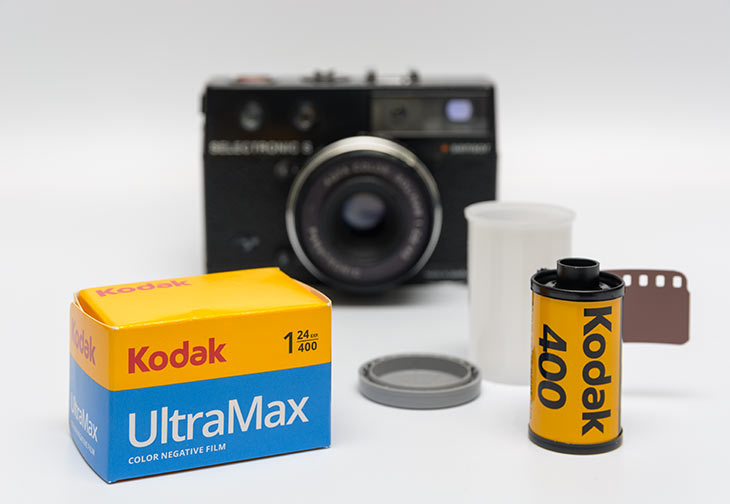 Eine Analogkamera sowie der Film Kodak Ultramax 400 nebst Schachtel stehen vor weißem Hintergrund.