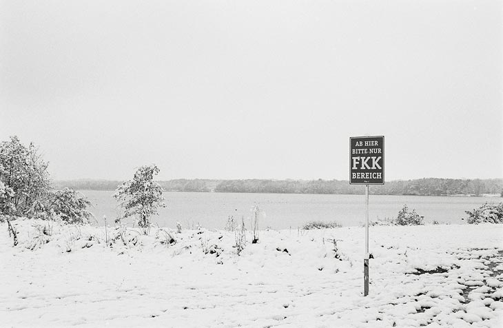minimalistische Schneelandschaft mit See und FKK-Schild